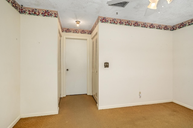 corridor with visible vents, baseboards, light colored carpet, and a textured ceiling