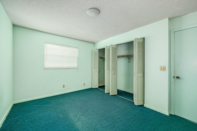 unfurnished bedroom featuring multiple closets, dark carpet, and a textured ceiling