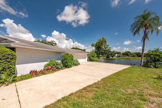 exterior space with a water view, a lawn, concrete block siding, a garage, and driveway