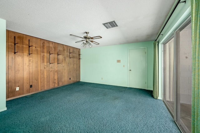 empty room with wood walls, dark colored carpet, a textured ceiling, and ceiling fan