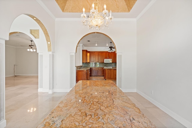 interior space featuring tasteful backsplash, light stone counters, ceiling fan with notable chandelier, crown molding, and decorative light fixtures