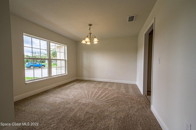 carpeted spare room with an inviting chandelier and a textured ceiling