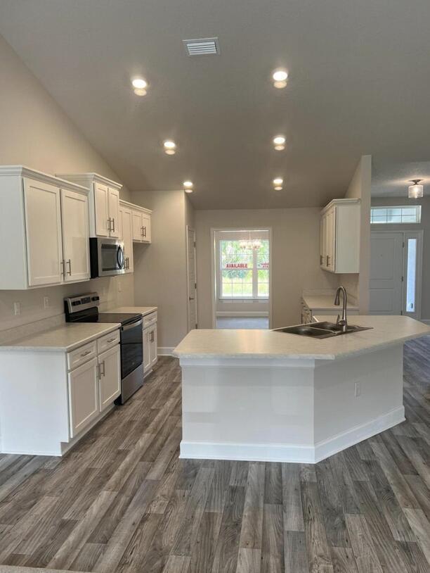 kitchen featuring dark wood-type flooring, vaulted ceiling, white cabinets, appliances with stainless steel finishes, and sink