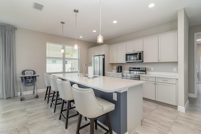 kitchen featuring white cabinetry, a kitchen breakfast bar, hanging light fixtures, a kitchen island with sink, and stainless steel appliances