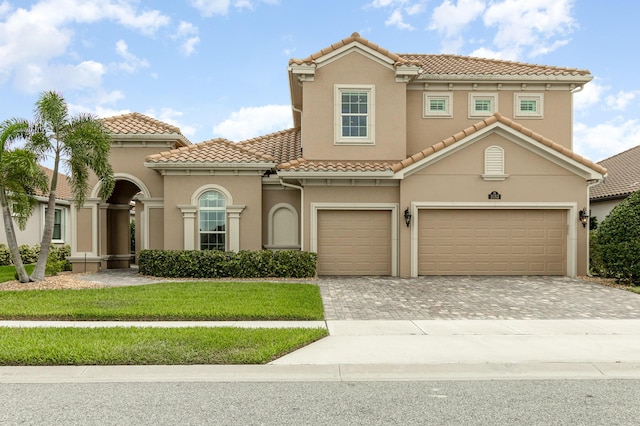 mediterranean / spanish-style house with a front yard, decorative driveway, a tiled roof, and stucco siding