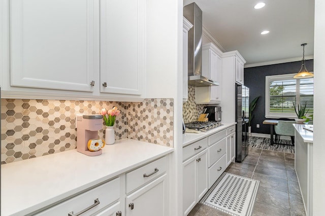 kitchen featuring stainless steel appliances, white cabinetry, light countertops, wall chimney exhaust hood, and crown molding