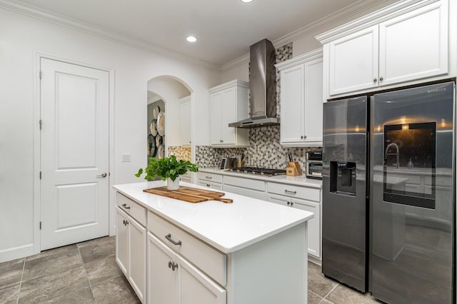 kitchen featuring black refrigerator with ice dispenser, ornamental molding, wall chimney exhaust hood, white cabinets, and stainless steel gas stovetop