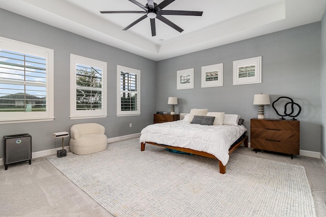 bedroom featuring ceiling fan, light colored carpet, and a tray ceiling