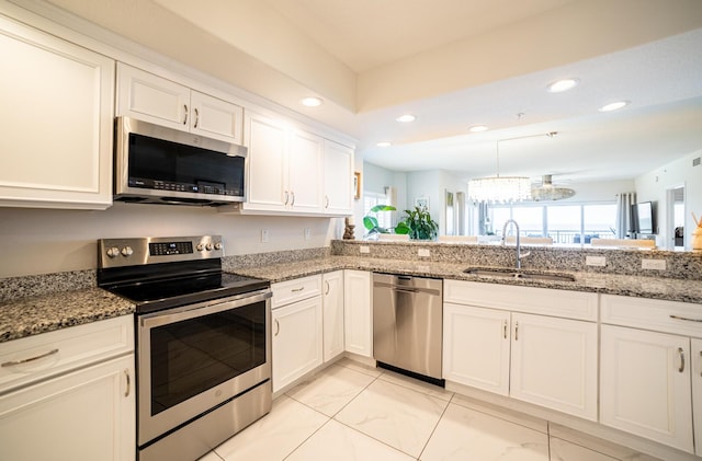 kitchen with appliances with stainless steel finishes, sink, an inviting chandelier, stone counters, and white cabinets