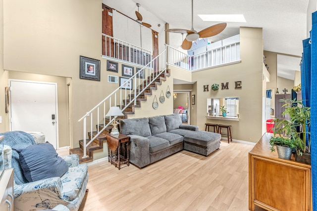 living room featuring high vaulted ceiling, a skylight, ceiling fan, and light hardwood / wood-style floors