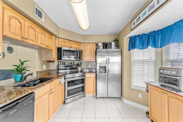 kitchen with appliances with stainless steel finishes, light brown cabinetry, dark stone countertops, and sink