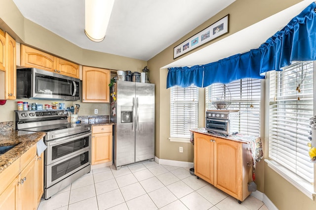 kitchen featuring light brown cabinetry, stainless steel appliances, dark stone counters, and light tile patterned flooring