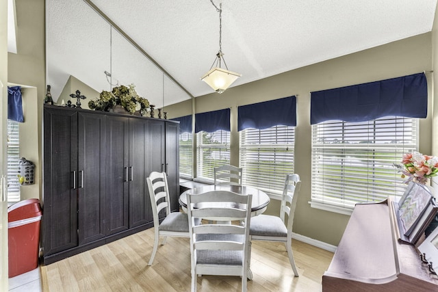 dining area featuring vaulted ceiling, a textured ceiling, and light hardwood / wood-style flooring