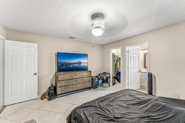 tiled bedroom featuring a textured ceiling, a spacious closet, ceiling fan, a closet, and ensuite bath