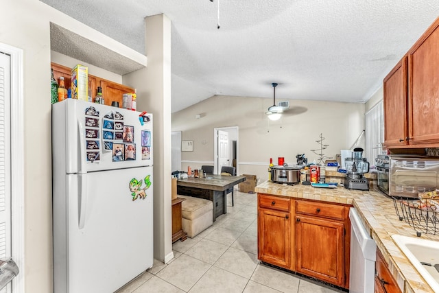 kitchen with ceiling fan, white appliances, tile countertops, light tile patterned floors, and lofted ceiling