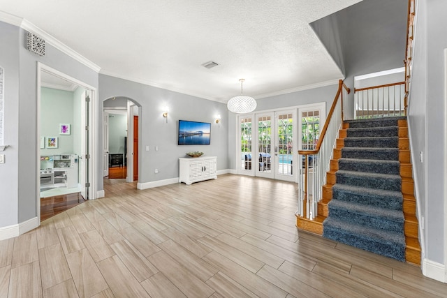 unfurnished living room with french doors, a textured ceiling, and ornamental molding