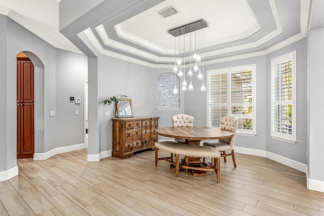 dining space featuring an inviting chandelier, a raised ceiling, crown molding, and light hardwood / wood-style flooring