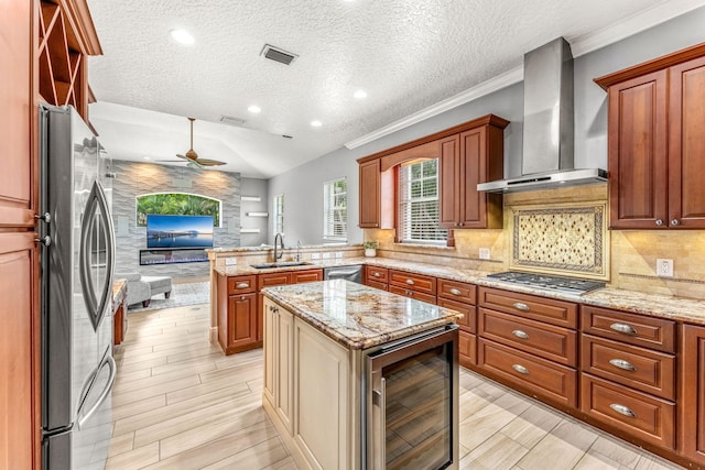 kitchen with stainless steel appliances, sink, a center island, wall chimney exhaust hood, and ceiling fan