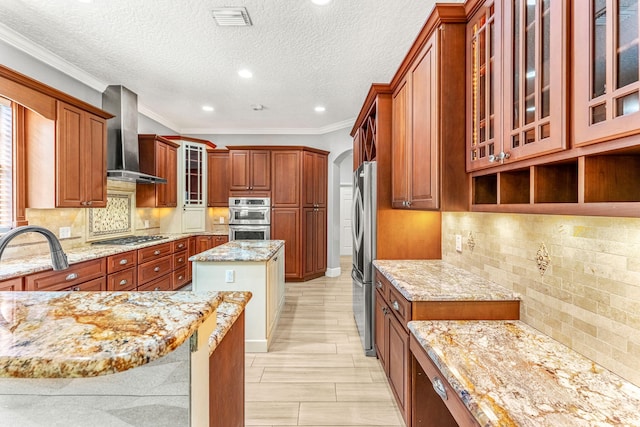 kitchen with light stone counters, wall chimney exhaust hood, a kitchen island, backsplash, and appliances with stainless steel finishes