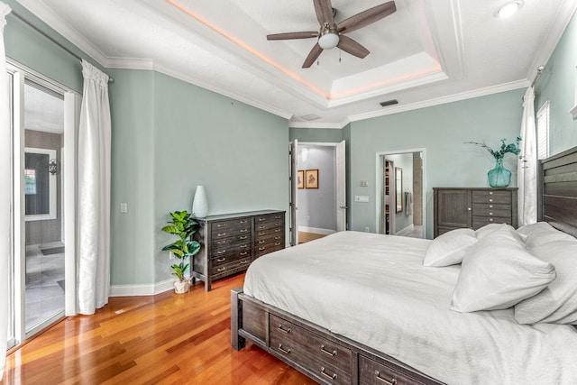 bedroom featuring a raised ceiling, hardwood / wood-style floors, connected bathroom, ceiling fan, and ornamental molding