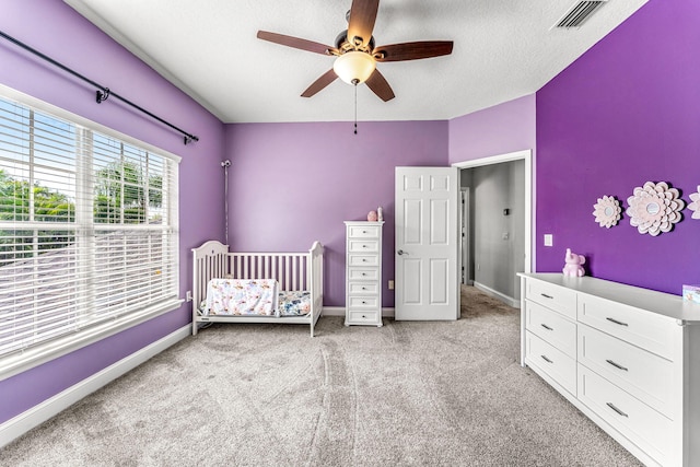 carpeted bedroom featuring a crib, a textured ceiling, and ceiling fan