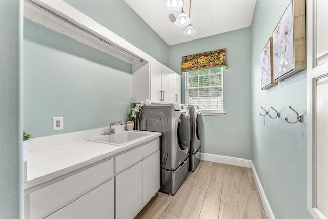 clothes washing area with separate washer and dryer, light hardwood / wood-style floors, cabinets, and sink