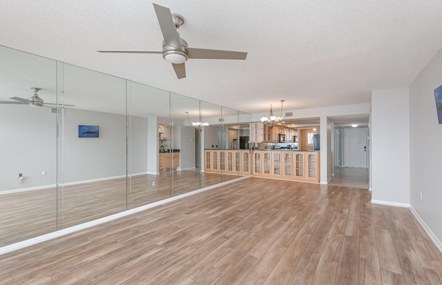 unfurnished living room with ceiling fan with notable chandelier, a textured ceiling, and light hardwood / wood-style flooring