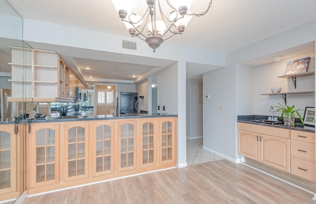 interior space featuring light brown cabinets, light wood-type flooring, a textured ceiling, an inviting chandelier, and appliances with stainless steel finishes