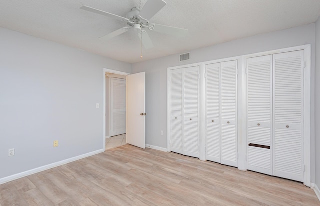 unfurnished bedroom featuring multiple closets, a textured ceiling, light wood-type flooring, and ceiling fan