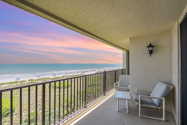 balcony at dusk with a water view and a view of the beach