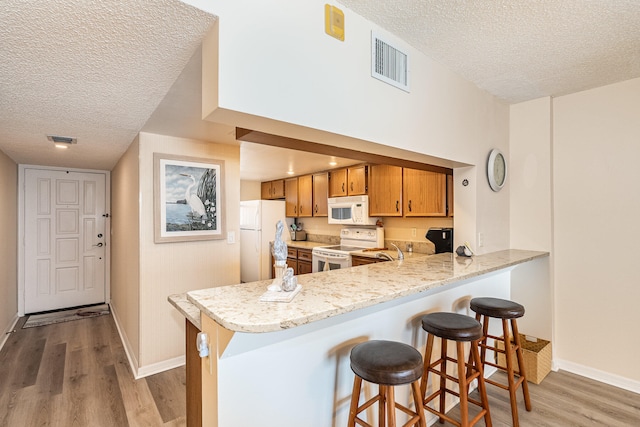 kitchen with kitchen peninsula, white appliances, light wood-type flooring, and a textured ceiling