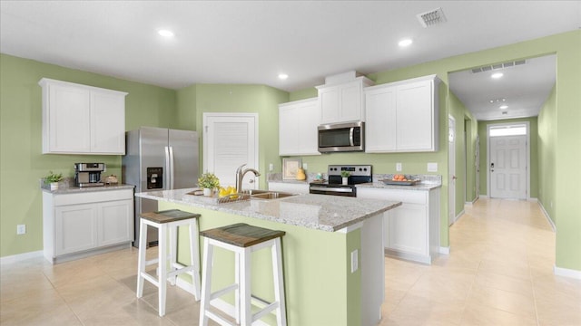 kitchen featuring a kitchen bar, sink, a center island with sink, appliances with stainless steel finishes, and white cabinets