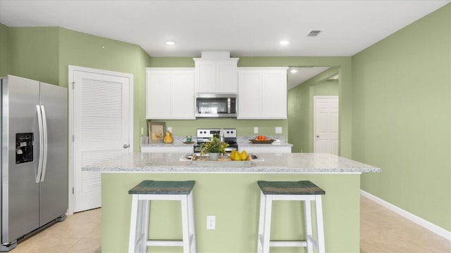 kitchen with a center island with sink, light stone countertops, white cabinets, and appliances with stainless steel finishes