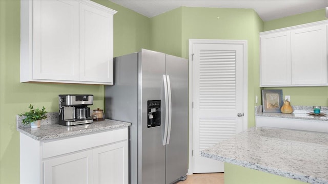 kitchen with stainless steel fridge, light stone countertops, and white cabinets