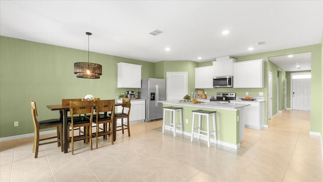 kitchen featuring a breakfast bar area, white cabinetry, decorative light fixtures, appliances with stainless steel finishes, and a kitchen island with sink