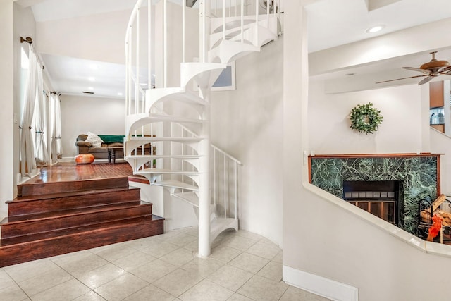 staircase with tile patterned flooring, ceiling fan, and a fireplace