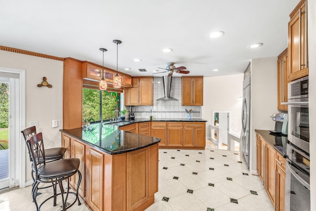 kitchen featuring a breakfast bar, pendant lighting, sink, stainless steel appliances, and wall chimney exhaust hood