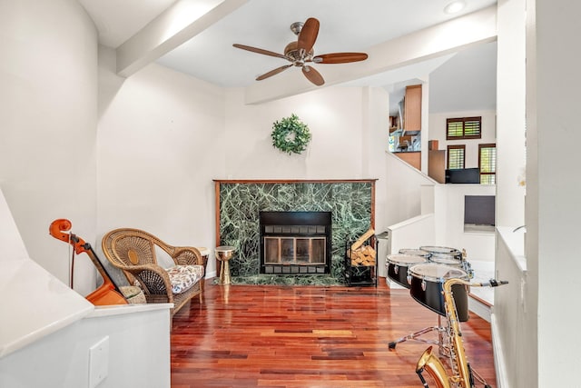 sitting room with ceiling fan, a premium fireplace, hardwood / wood-style floors, and beam ceiling