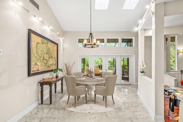 dining area with a high ceiling, a skylight, a notable chandelier, and french doors