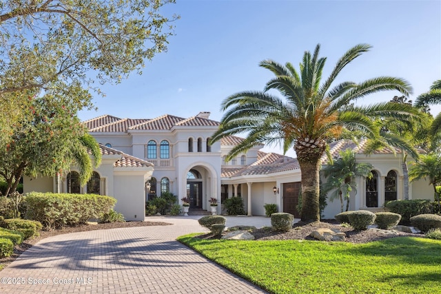 mediterranean / spanish house featuring a tile roof, stucco siding, french doors, decorative driveway, and a garage