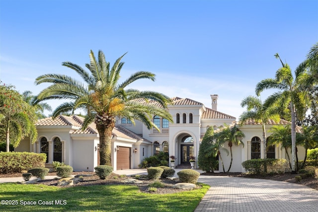 mediterranean / spanish-style home with a tiled roof, stucco siding, french doors, and decorative driveway