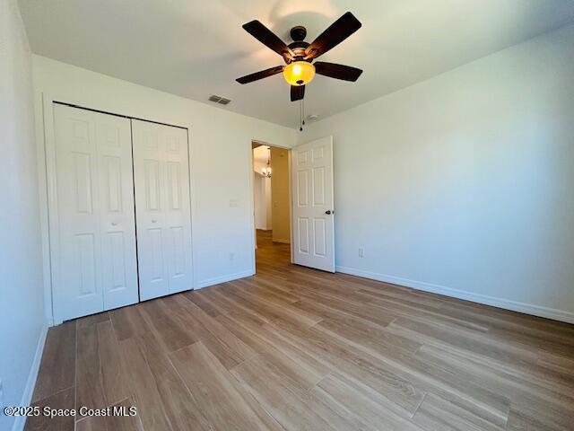 unfurnished bedroom featuring visible vents, ceiling fan, baseboards, light wood-style floors, and a closet