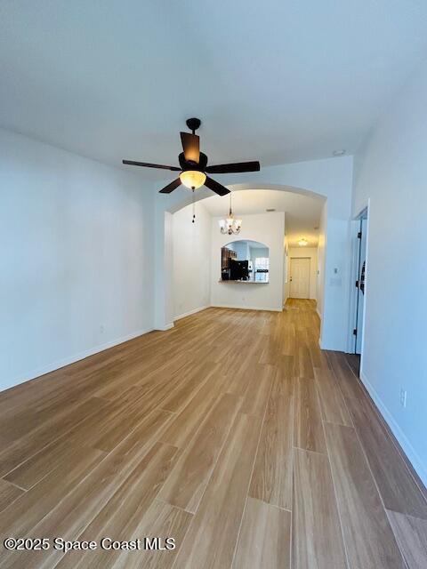 unfurnished living room with light wood-type flooring, baseboards, arched walkways, and ceiling fan with notable chandelier