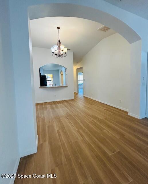 unfurnished living room with a chandelier, lofted ceiling, baseboards, and wood finished floors