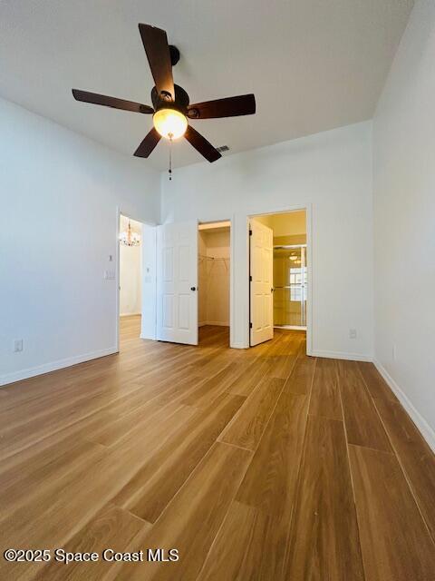 unfurnished bedroom featuring a walk in closet, baseboards, visible vents, and wood finished floors