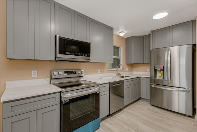 kitchen featuring stainless steel appliances, light wood-type flooring, sink, light stone counters, and gray cabinetry