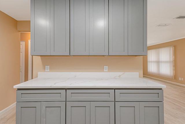 kitchen with light stone counters, light wood-type flooring, crown molding, and gray cabinets