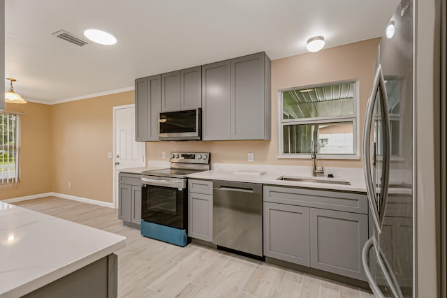 kitchen featuring light hardwood / wood-style floors, hanging light fixtures, appliances with stainless steel finishes, sink, and gray cabinetry