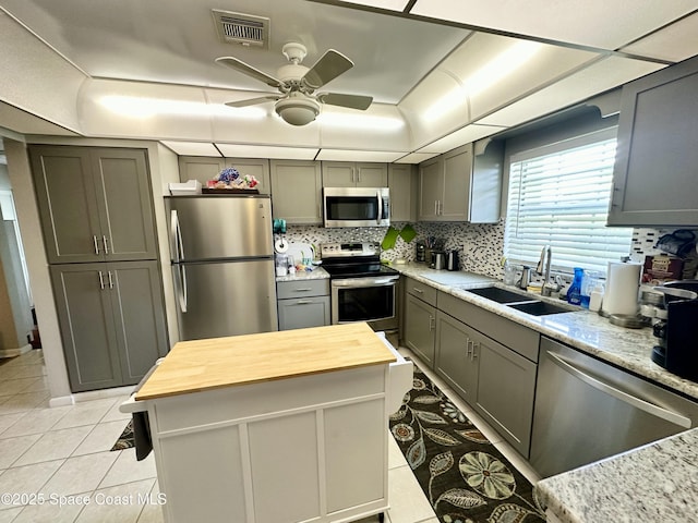 kitchen featuring appliances with stainless steel finishes, wood counters, sink, a center island, and light tile patterned floors