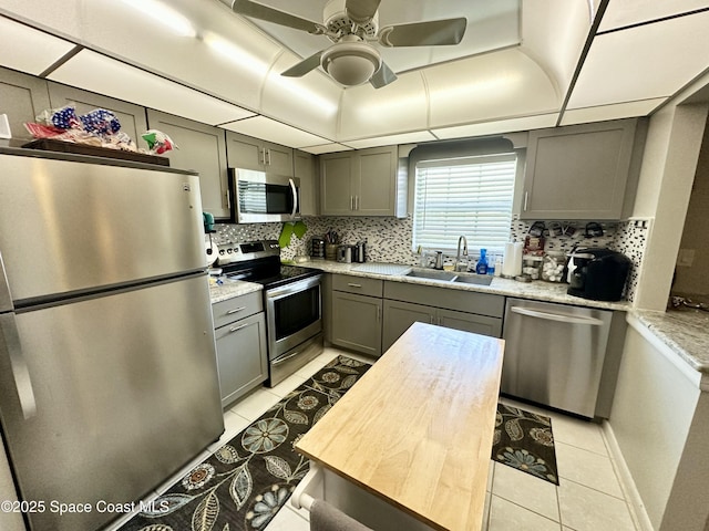 kitchen featuring sink, ceiling fan, stainless steel appliances, light stone counters, and light tile patterned flooring